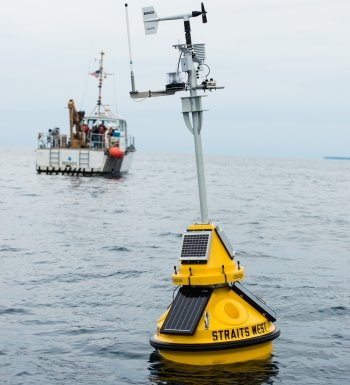 A Michigan Tech buoy floats in the waters of the Straits of Mackinac, with the research vessel Osprey in the background.