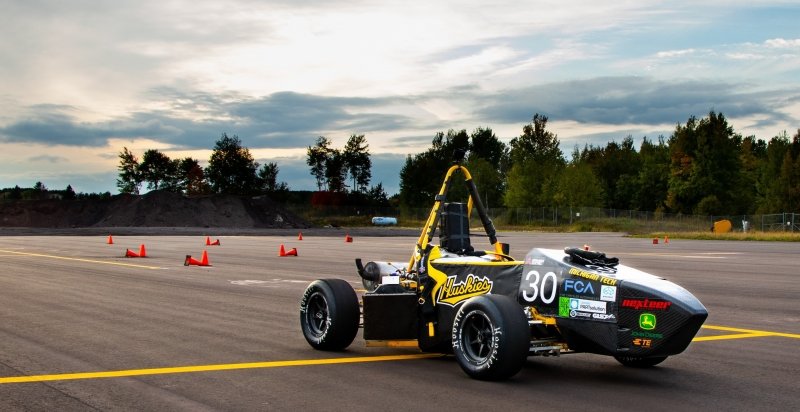 A formula collegiate design car with a Huskies sticker on it in September at a test track with a yellow line and blue sky in the background