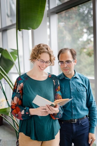 two people smiling and looking down at a book in their hands