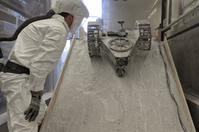Student in protective gear stands in a sealed lunar test chamber with a rover.