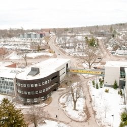 Michigan Tech College of Computing banner and an aerial view of a snowy campus exterior with sidewalks and the highway and hill in the distance.