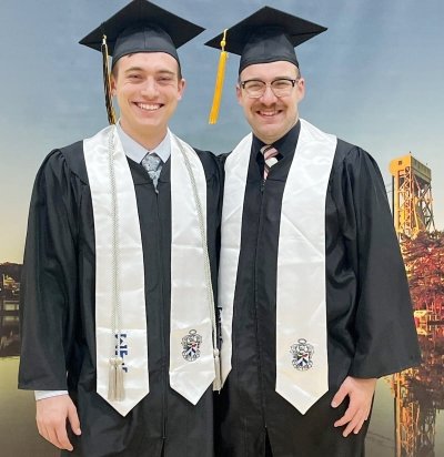 Two Michigan Tech grads stand in front of a banner of the Portage Lake Lift Bridge at spring 2022 commencement.