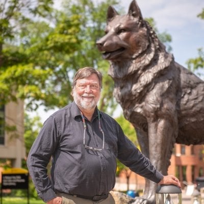 Mike Mullins stands in front of the husky statue.