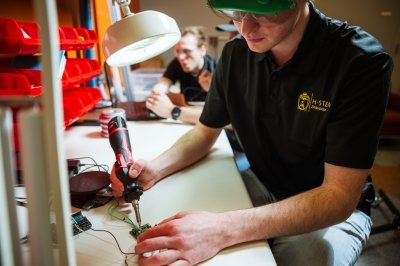 Michigan Tech's H-STEM Enterprise team works on a project in the lab that involves welding a circuit board for a medical device.