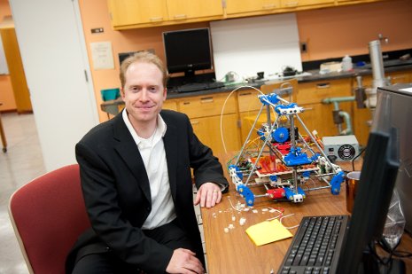 Joshua Pearce with a Mendel RepRap 3D printer. The machine is made up of parts from any hardware store, open-source electronics and parts that it can make for itself--all the red, white and blue components.