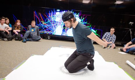 Orrico kneels on a large piece of paper, creating a piece of art while his movements are tracked by Tech's Mind Music Machine Lab researchers.