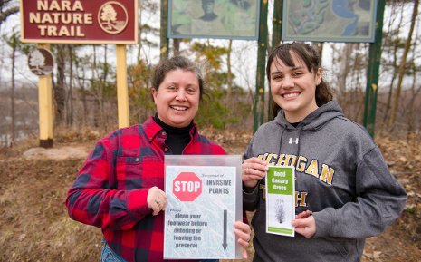 Meral Jackson, left, and Krysten Cooper, with a sample of the sign and brochure that Krysten designed to prevent the spread of reed canary grass at Nara Nature Park. The actual signs will be larger, brighter, sturdier, and mounted on posts.