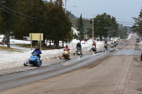 Snowmobiles driving along the side of a road.