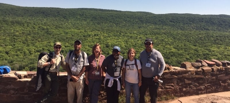 Six teachers in hiking gear on Keweenaw Peninsula's Brockway Mountain with a Rock wall behind them.