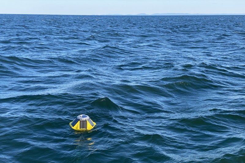 A Spotter buoy in the water with the Huron Mountains on the horizon.