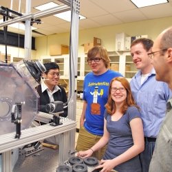 Four Grad students talking with faculty in a physics lab with small cloud chamber