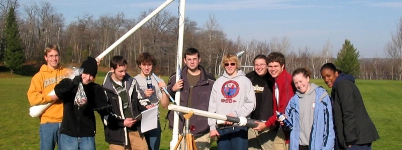 Ten students in the field posing for a photograph with potato guns after measuring the physics after potatoes are projected.