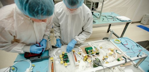 Two individuals working on aerospace/satellite components