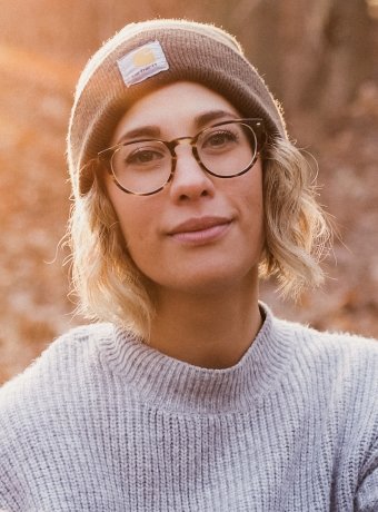 Debbie Paver wears glasses and dons a Carhartt beanie in front of a blurred natural background.