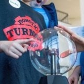 Young student in a steam punk hat touching an electricity globe.