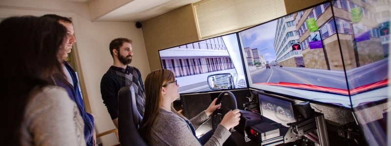 Participant sitting at a driving research machine while researchers look on as the participant drives.