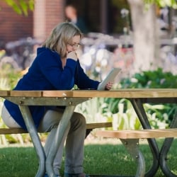 Woman sitting at a picnic table reading on a tablet