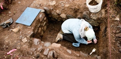 Student inside an excavation square section collecting artifacts