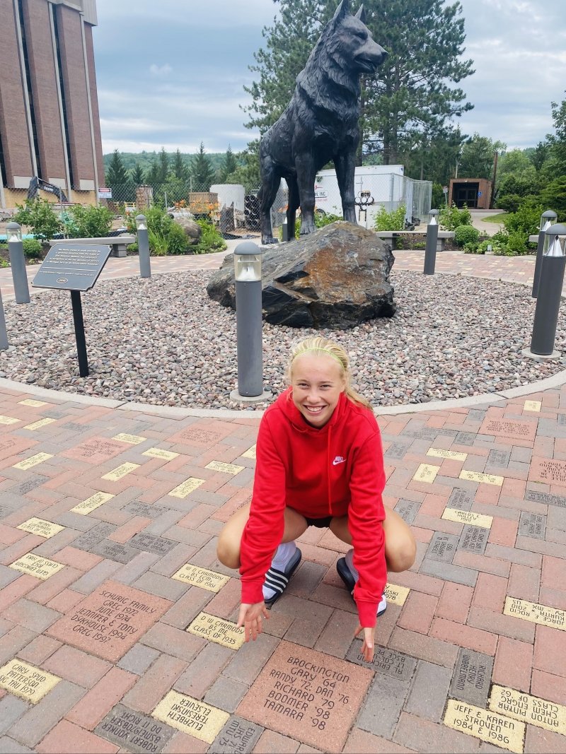 A Husky starting Tech in fall 2023 poses with her Brockington family plaque in Husky Plaza on Campus.