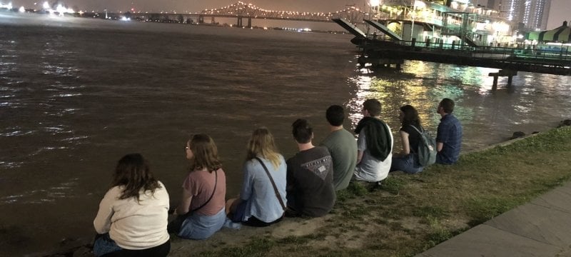 Students sitting at the side of a river.