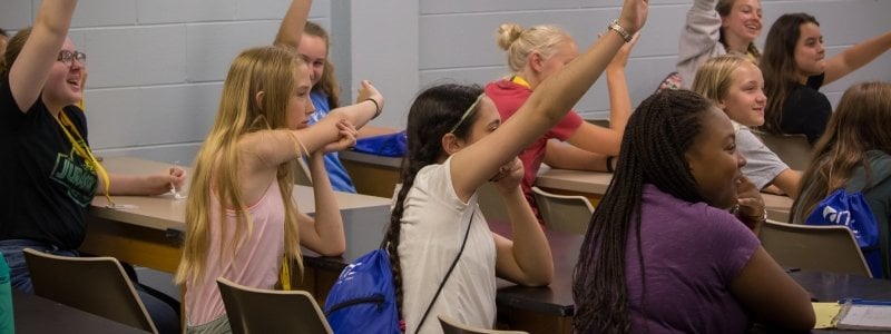 A classroom of young women with their hands raised.
