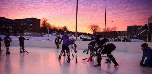 Students playing broomball with a sunset in the background.