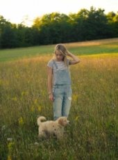 A young woman stands in a field looking down at a puppy.