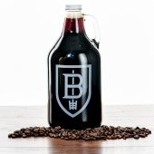 A growler of dark beer with coffee beans scattered in front of it.