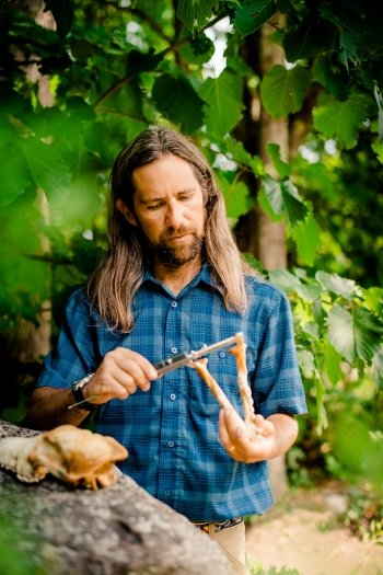 John Vucetich holds a caliber and a wolf mandible. A wolf skull sits on a rock in the left foreground.