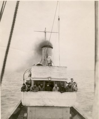 A black and white 1918 photo of men on the bridge of a ship steaming out to sea with lake superior in the background