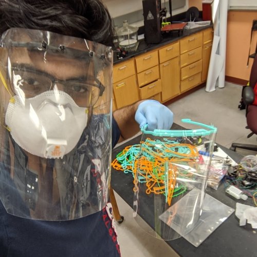 man in face mask and 3D printed face shield with other shields being assembled in an open source lab at Michigan Tech.