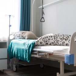 a home hospital bed with handhold, a colorful graphic geometric quilt and a window in the background.