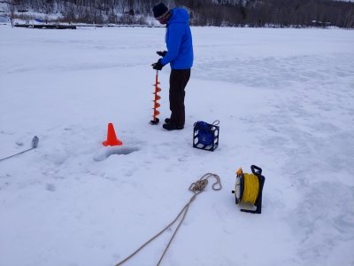 A student in a jacket and bundled up for winter with a face mask deploys and auger on the frozen Keweenaw waterway which is covered in snow in winter.