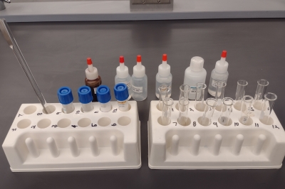 A neatly arranged set of vials, bottles, stir spoons and empty containers sitting on a laboratory benchtop.