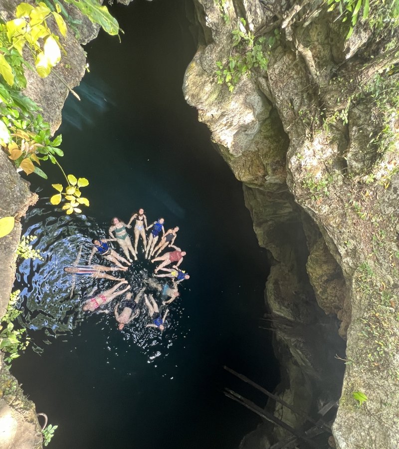 A group floats in a Yucatan cenote, or sinkhole, as seen from above, in a circle shape.