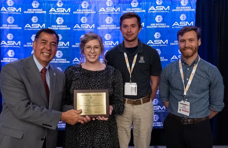 An industry leader presents three MTU students with a plaque at the ASM International Design Competition in 2022.