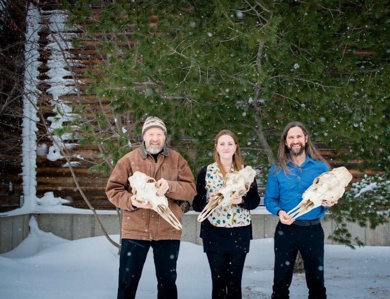 Co-leaders of the Isle Royale wolf-moose study stand outside the Michigan Tech College of Forest Resources and Environmental Sciences. They are holding moose skulls as the snow gently falls on a winter day.