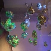 An installation hanging from the ceiling of aluminum foil crafted into flower petals, with light shinning on them to create colors.