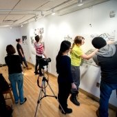 Students work on large drawings on the studio walls with a camera recording.