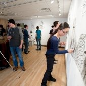 Students work on their drawings on the studio wall while others observe.