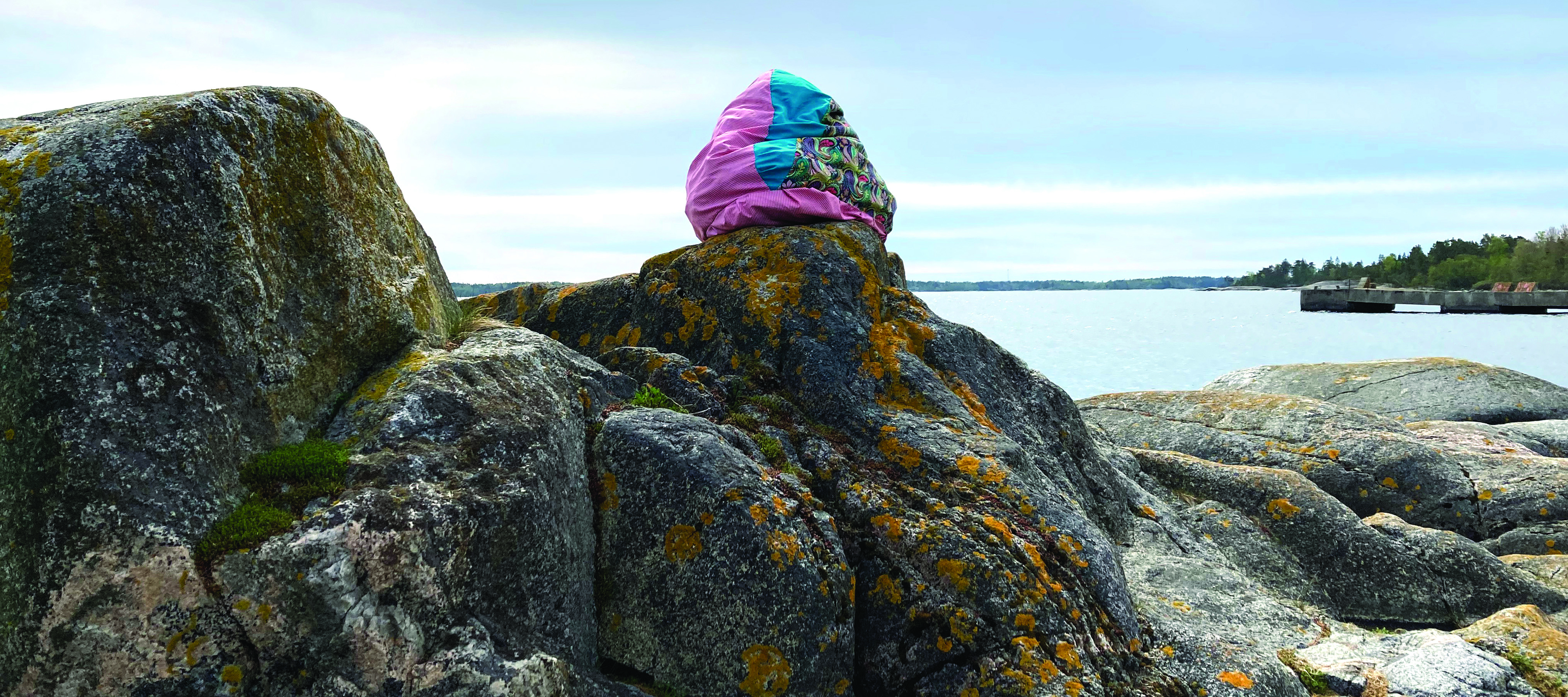 A soft, bright sculpture sitting on a rock in front of water
