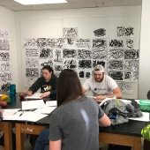 Students sitting around a workbench painting.
