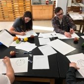 Students sitting around a work table drawing fruit