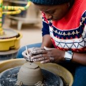 Student sitting at a pottery wheel using a tool to sculpt clay