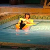 An actor performing inside a pool on a float with a hat and sunglasses on the stage of the McArdle Theatre.