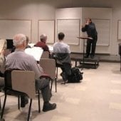 Conductor leading a seated choir in the Choral Rehearsal Room.