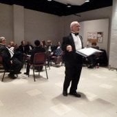 The conductor standing, preparing, before a performance in dress attire in the Choral Rehearsal Room.