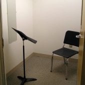 Inside one of the practice rooms that has a music stand and chair.
