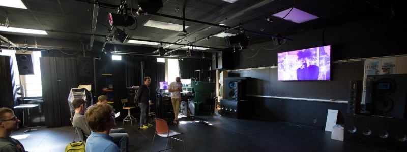 Students sitting inside the Lighting and Sound Lab viewing a performance on the television.