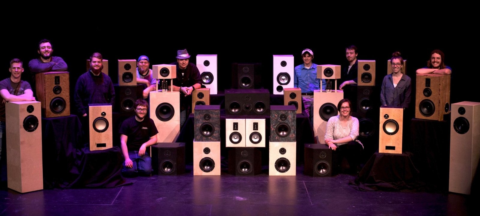 Students standing and kneeling next to speakers of various sizes and design